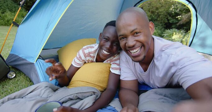 African American father and teenage son after laughing, reaching and taking selfie in blue tent
