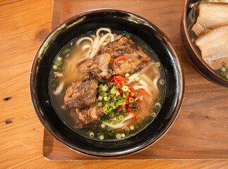 Traditional Okinawa Soba noodle soup with pork belly and ribs in a black bowl.
