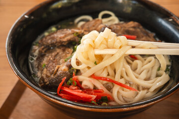Traditional Okinawa Soba noodle soup with pork belly and ribs in a black bowl.