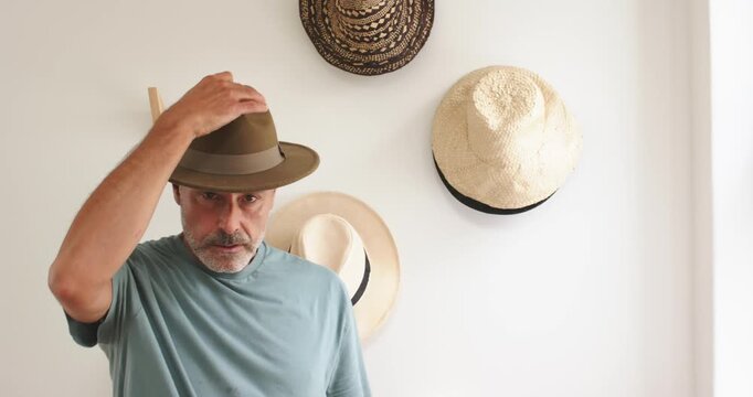 Mature man picking brown-green fedora from hat display, inspecting fit and adjusting hat on head