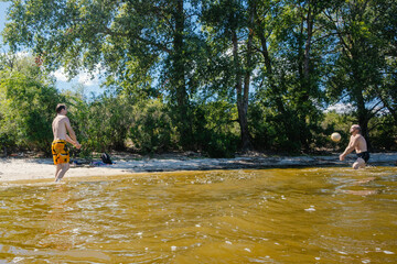 Fototapeta premium Two Friends Playing Beach Volleyball in River Water on Sunny Summer Day