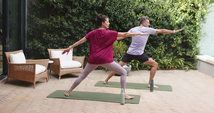 Yoga partners starting placing feet lowering into Warrior II practicing balance on mats on patio