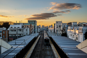 Symmetrical perspective of a commuter train on the railway tracks at Shiinamachi Station during a glowing golden hour sunset in Tokyo, Japan © ghendrak