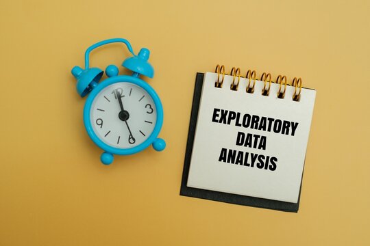 Blue alarm clock next to a notepad with EXPLORATORY DATA ANALYSIS text on a yellow background. Concept for data science, time management, research deadline and analytical workflow