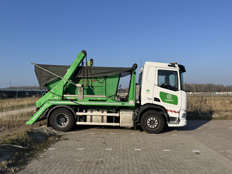 Almere, the Netherlands - March 22, 2026:  DAF XD skip loader with a secured green container against a clear blue sky.