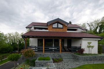 Fototapeta premium Modern suburban house with covered porch, stone steps and landscaped front garden under cloudy sky