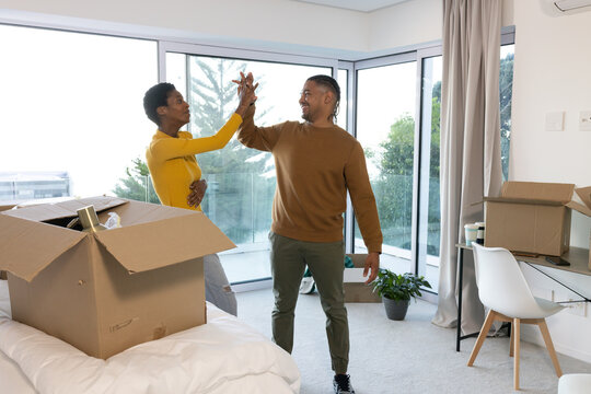 High-fiving Diverse couple celebrating in newly occupied apartment living area, with moving boxes