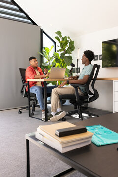 Talking Diverse male coworkers sharing ideas at desk in meeting room, with laptop and microphone