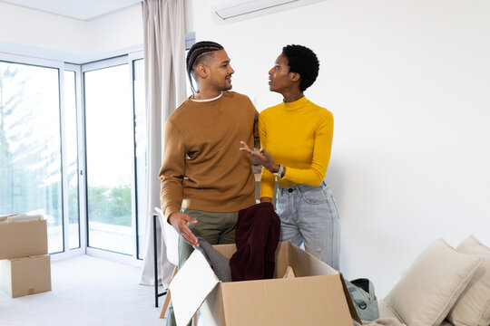 Unpacking Diverse couple sorting folded clothing in living room, with cardboard moving boxes