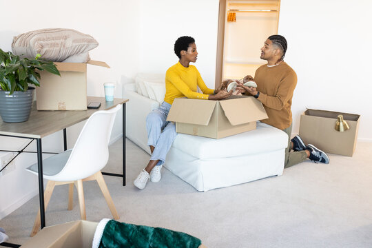 Unpacking Diverse couple unpacking moving boxes in home living room, with potted plant, coffee cup
