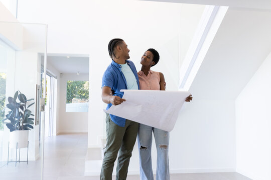 Reviewing Diverse couple holding blueprint in modern home entryway, with home design theme