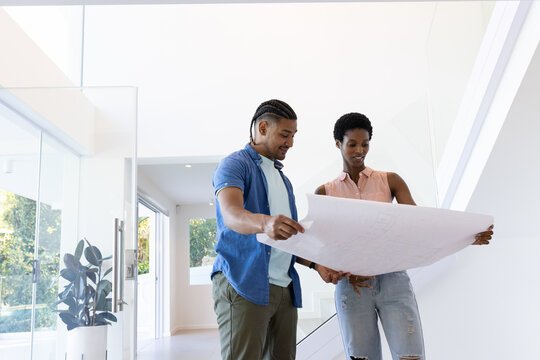 Couple examining architectural blueprint in modern home foyer, with glass staircase