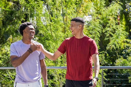 Diverse male friends fist bumping on terrace in front of foliage, with metal railing and bracelets