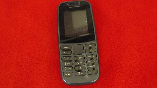 Extreme closeup of old vintage keypad mobile phone with finger dialling physical number button for calling. Nostalgic 90s technology portable and wireless communication equipment.