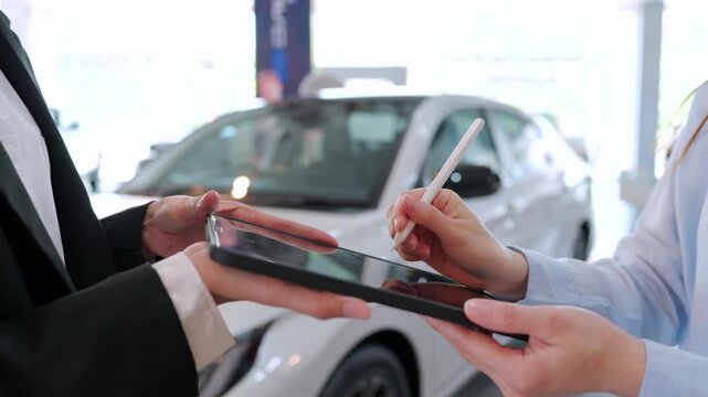 Close-up of Asian woman signing digital signature on tablet using a stylus in showroom. Successful car purchase agreement. Modern paperless automotive business concept.