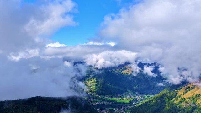 Drone 4K timelapse of fast-moving clouds revealing an alpine valley landscape with forests and mountain scenery. Dynamic atmospheric motion creates a dramatic and cinematic natural scene.
