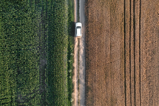 Aerial view of a lone white vehicle traverses a dusty path between verdant fields and sun-scorched earth, Chyhyrynskyi district, Cherkasy Oblast, Ukraine.