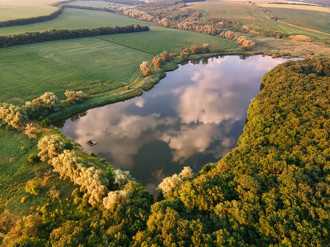 Aerial view of the lake reflecting the sky, surrounded by lush green fields and dense forests, Chyhyryns kyi district, Cherkasy Oblast, Ukraine.