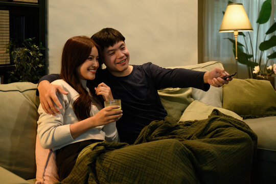 Young couple cuddling under a blanket while using a remote control, creating a warm and comfortable lifestyle scene