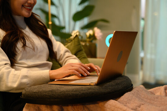 Close-up of an Asian woman typing on a laptop while sitting comfortably at home, representing remote work and digital nomad lifestyle