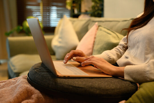 Detail shot of hands using a laptop on a sofa, showing modern domestic life, productivity, and flexible work from home