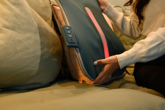 Detailed view of a woman adjusting an ergonomic back massager, highlighting comfort, posture support, and home wellness