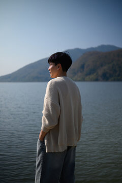 Lifestyle portrait of a young man relaxing near water with mountains in the background, expressing calmness and freedom