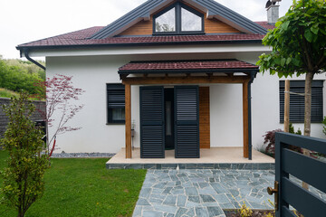 Fototapeta premium Modern suburban house entrance with covered porch, shutters, stone pathway and landscaped front garden