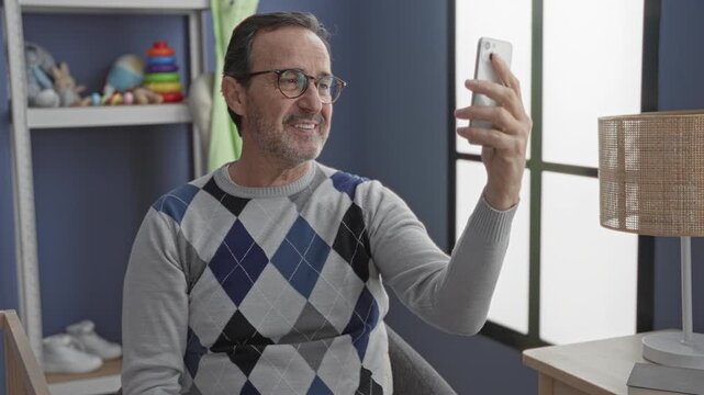 Man holding smartphone with outstretched arm in studio baby room near crib and toys; family connection warmth.