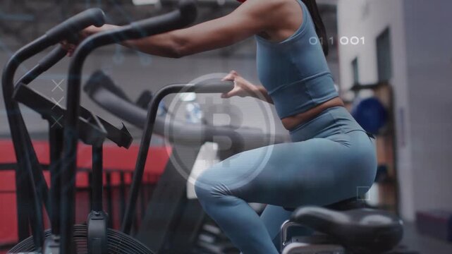 Female fitness-goer pedaling air bike in gym, pedal motion starting crypto overlay tracking workout