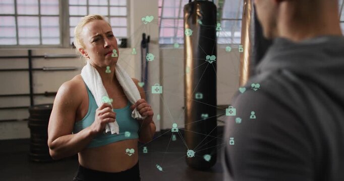 Woman with towel speaking to coach in gym, starting green health icons forming network for feedback