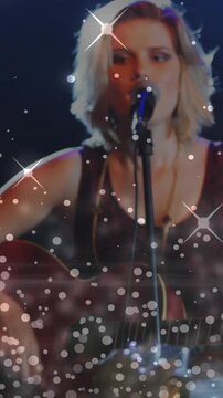 Vertical video: Singing teen strumming guitar with cam widening on stage mic, rim light and sparkle