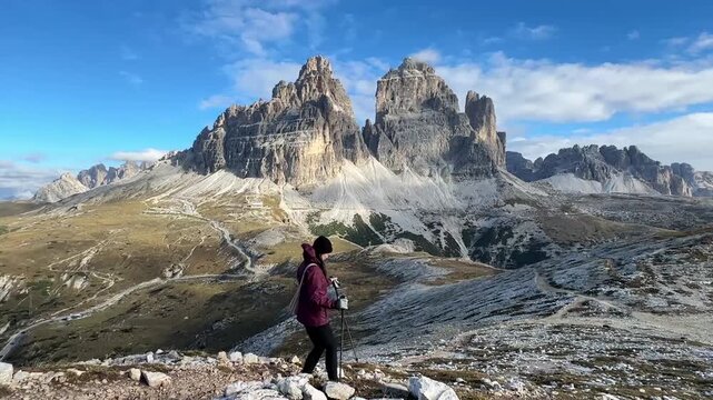 Woman stands before Tre Cime di Lavaredo in the Dolomites during soft morning light, with towering peaks, alpine terrain and a peaceful atmosphere highlighting scale and natural beauty