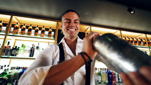 Smiling professional bartender shaking a cocktail at a stylish bar counter, creating drinks with expertise and passion