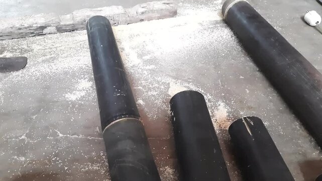 Workshop process showing dark cylindrical materials being cut and generating sawdust footage