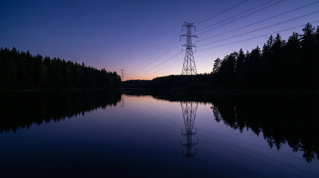 High voltage transmission tower reflected in calm forest lake at twilight