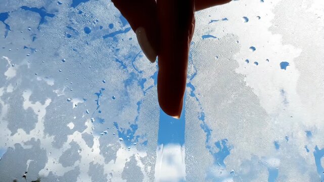 A finger drawing a clear line on a fogged window glass, revealing the blue sky and clouds behind, symbolizing clarity, vision, and new perspective