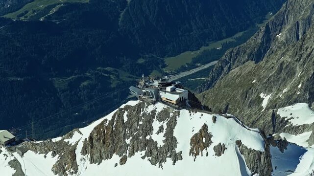Summit station building located at the top of Aiguille du Midi in the French Alps near Chamonix, set against a vast, clear blue sky and rugged high-altitude snowy mountain peaks