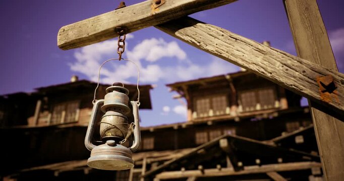 A rustic lantern is suspended from a wooden beam, surrounded by a weathered building. The clear sky and vintage architecture create a charming atmosphere.