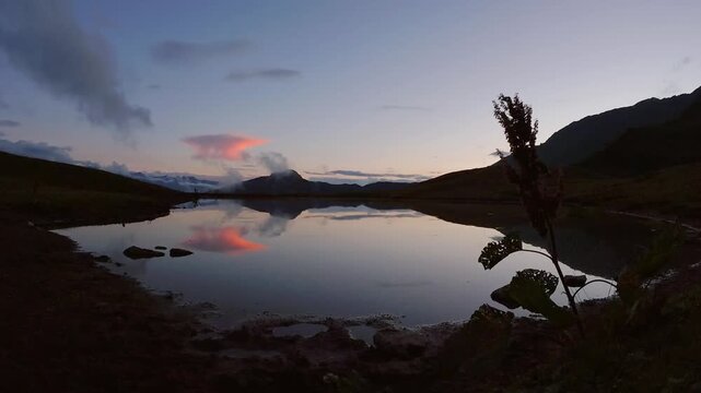 Zoom in view mesmerizing sunset timelapse at Koruldi Lakes, Georgia. The calm water mirrors the Greater Caucasus peaks and fiery clouds in a perfect alpine reflection