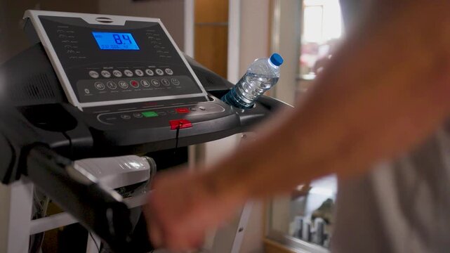 Man pressing red stop button on treadmill console after workout. Close-up of a hand pushing the emergency stop button on a treadmill control panel. Concept of finishing a cardio session and safety