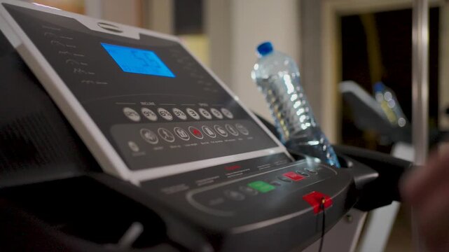 Man pressing red stop button on treadmill console after workout. Close-up of a hand pushing the emergency stop button on a treadmill control panel. Concept of finishing a cardio session and safety