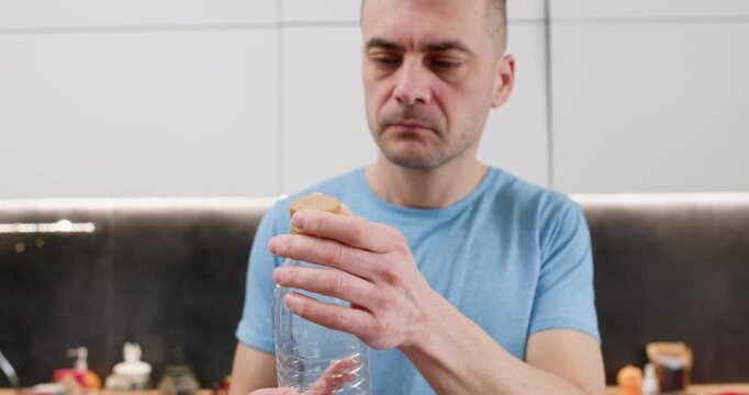 Thoughtful man studies plastic bottle touching cap before recycling step begins. Person checks container shape deciding separating lid for proper sorting