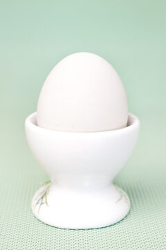 White chicken egg in ceramic egg cup on blue green background vertical macro front view
