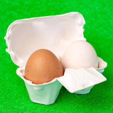 Brown and white fresh eggs inside cardboard paper package on green  fake grass background macro