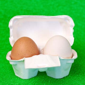 Brown and white fresh eggs inside cardboard box package on green  fake grass background front view