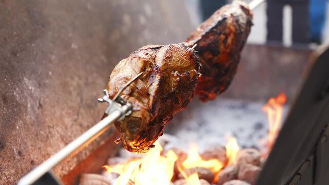 Cooking meat on a spit over open flames at an outdoor grill during a sunny afternoon in a backyard setting