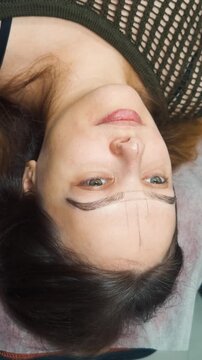 Young female client receiving beauty service, getting eyebrow shaping and definition with hairstroke technique before cosmetic tattooing process for natural looking, fuller brows