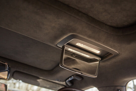 Car roof console close-up with integrated mirror and interior lights on a modern vehicle headliner, clean automotive detail in soft daylight