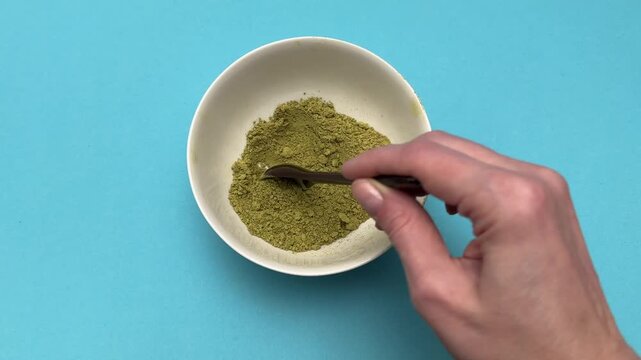 Woman stirs henna powder with spoon in bowl closeup
